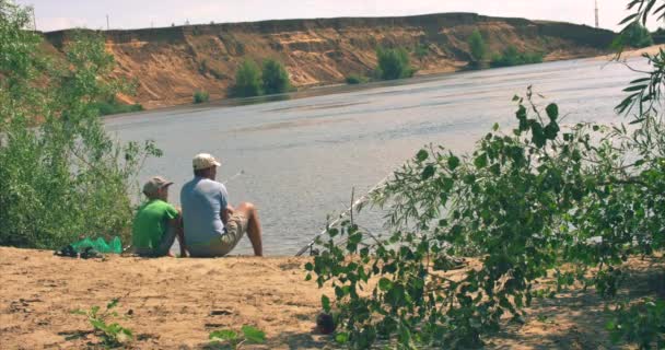 Feliz padre e hijo están sentados en la orilla del río, la pesca, papá e hijo están pescando en la mañana. Familia feliz . — Vídeos de Stock