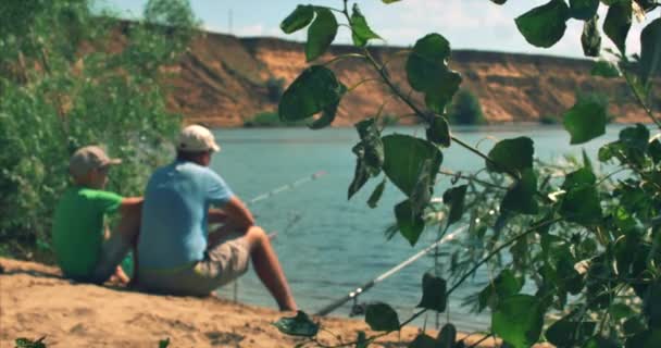 Feliz padre e hijo están sentados en la orilla del río, la pesca, papá e hijo están pescando en la mañana. Familia feliz . — Vídeos de Stock