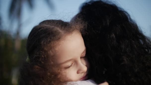 Daughter in the arms of the mother on the street and gives her a big hug, kissing and smiling look at the camera, close-up. Slow motion. — Stock Video