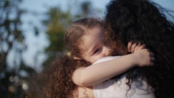 Córka w ramionach matki na ulicy i daje jej big hug, Całowanie i uśmiechając się patrzeć na aparat, szczelnie-do góry. Zwolnionym tempie. — Wideo stockowe