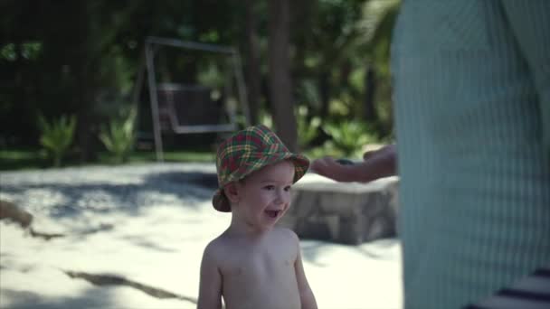 Glücklicher kleiner Junge mit Hut geht zu seiner Mutter auf den Sand, um sie mit Früchten zu behandeln. — Stockvideo