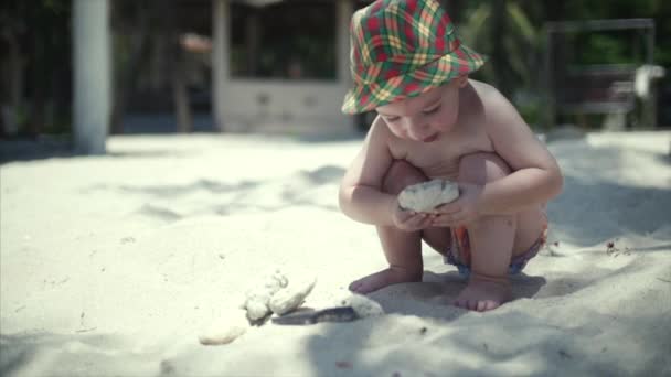 Gelukkige jongen in een hoed die spelen op het zand. — Stockvideo