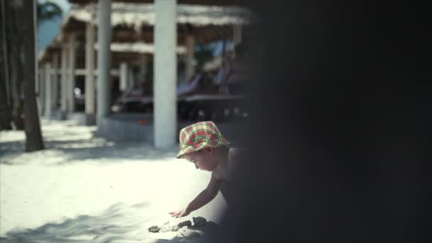 Lycklig pojke i en hatt som spelar på sanden. — Stockvideo