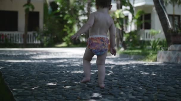 Menino de dois anos de idade caminha na praia de areia de verão nos trópicos ao longo da areia . — Vídeo de Stock