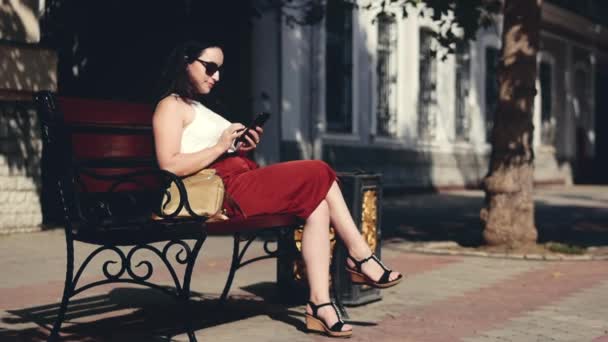 Όμορφη γυναίκα Καυκάσιος εμφάνιση χρησιμοποιώντας έξυπνο τηλέφωνο app τεχνολογίας κάθεται στους δρόμους της πόλης ένα πάγκο αστικών ευτυχισμένη Ζώντας — Αρχείο Βίντεο