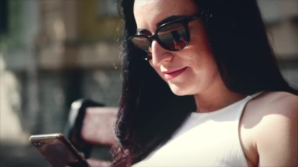 Красивая деловая женщина кавказского внешнего вида с помощью приложения смартфонов сидит на скамейке улиц города, живя городской счастливый образ жизни — стоковое видео