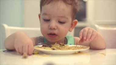 Küçük çocuk bir önlük bir masada oturan ve kendi spagetti yemek bebek yiyor isteyerek.