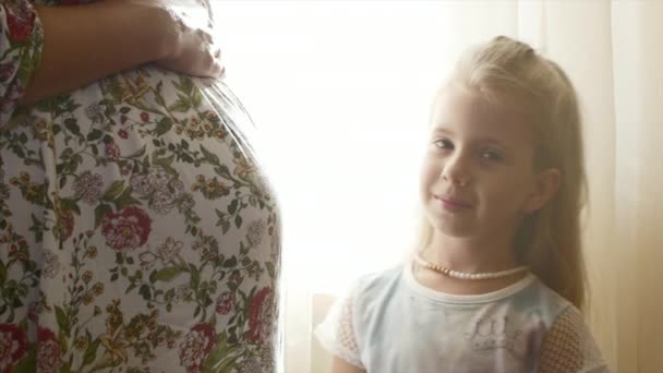 Mãe grávida está ao lado de sua filha, uma pequena filha olha nos olhos de suas mães, e depois abraça a mãe . — Vídeo de Stock