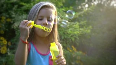 Güneşli bir günde sabun köpüğü üfleme mutlu küçük bir beyaz kız ağır çekim. Doğada kavramı mutlu çocukluk veya çocuk oyunları.