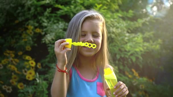 Movimento lento de uma menina caucasiana feliz soprando bolhas de sabão em um dia ensolarado. Conceito infância feliz ou jogos infantis na natureza . — Vídeo de Stock