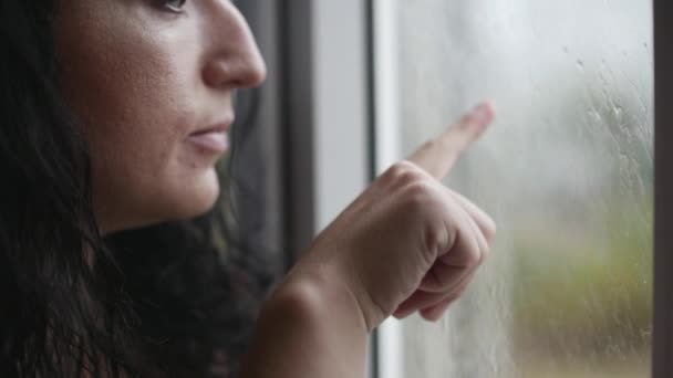 Mujer joven dibuja un corazón en una ventana empañada, sonriendo, fuera de la ventana en la calle su lluvia . — Vídeo de stock