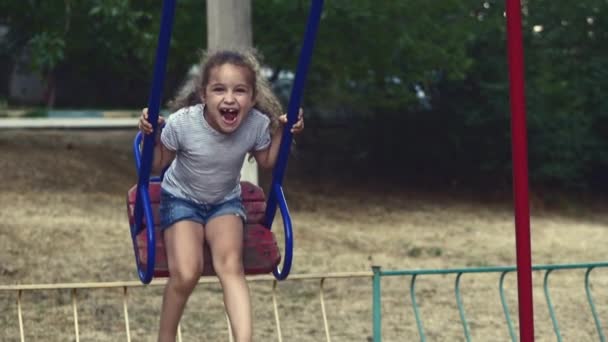 Happy young little girl spinning in a swing and smiling — Stock Video