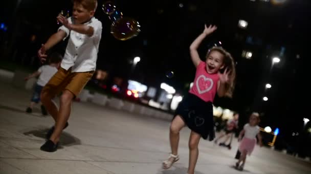 Fröhliche Kindergruppe, die im Park mit Seifenblasen spielt. Kinder fangen Seifenblasen am Abend im Park. — Stockvideo