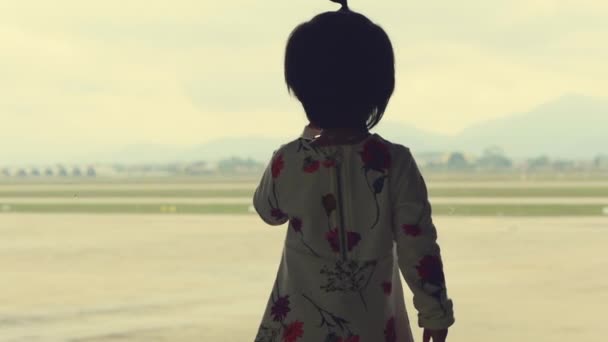 Al aeropuerto. Niña mira por la ventana con vista en la zona del aeropuerto . — Vídeo de stock