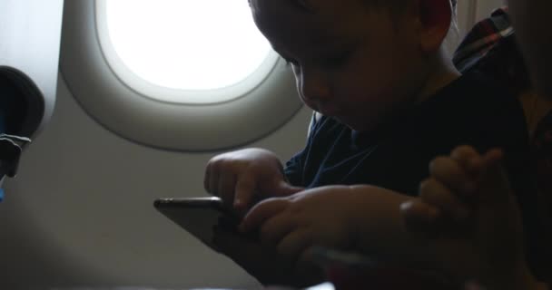 Avião está voando, o menino está sentado na mãe nas canetas e assistindo desenhos animados . — Vídeo de Stock
