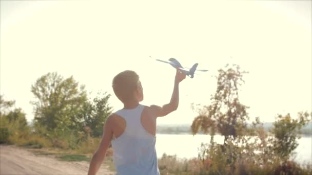 Glückliches Kind, das mit Flugzeug in den Händen spielt und vor dem Hintergrund des Sonnenuntergangs läuft. — Stockvideo