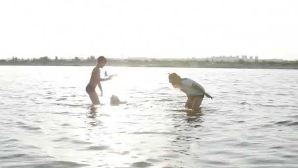 Infancia feliz y despreocupada. Los niños juegan con un perro, corren a lo largo de la arena, ríen, juegan en el río, lanzan un avión de juguete . — Vídeos de Stock