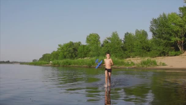 Infancia feliz y despreocupada. Los niños juegan con un perro, corren a lo largo de la arena, ríen, juegan en el río, lanzan un avión de juguete . — Vídeo de stock