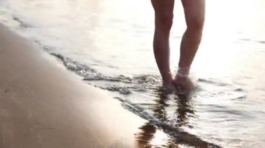 Üzerinden aşağıda kadınsı bacaklar görüntülemek, sahilde yürüyüş sahil, güzel erkek, bir kadın yürüyor. Denizin kadın ayaklarını yıkar.