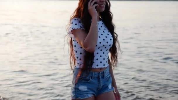 Jonge vrouw praten over de telefoon, lopen op het zand langs het strand. — Stockvideo