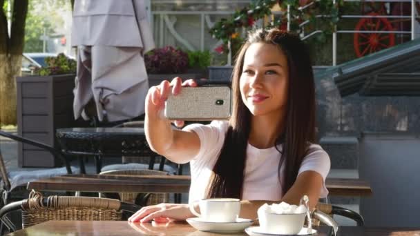 Ung, glad attraktiv kvinna dricka kaffe på ett café, tar selfies. — Stockvideo