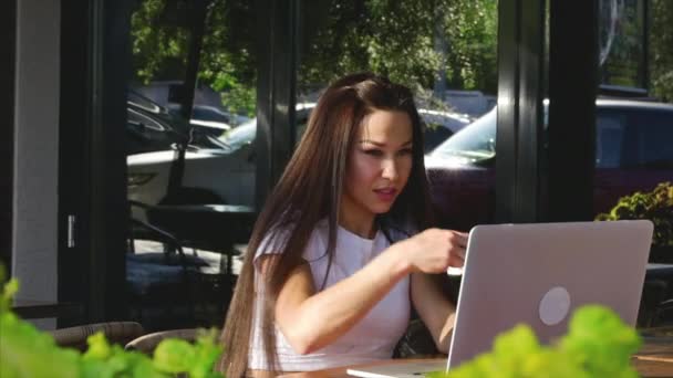 Joven, mujer atractiva feliz disfrutando de una taza de café en un café, escribiendo en un ordenador portátil . — Vídeos de Stock