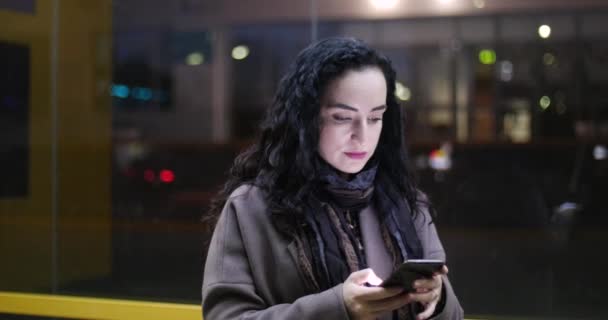 Attractive woman using mobile phone while walking through the streets on the background of festive lights of night city. — Stock Video