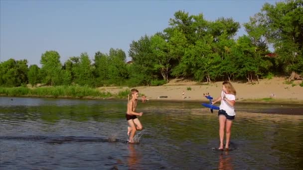 Infanzia felice e senza pensieri. I bambini giocano con un cane, corrono lungo la sabbia, ridere, giocare sul fiume, lanciare un aeroplano giocattolo . — Video Stock