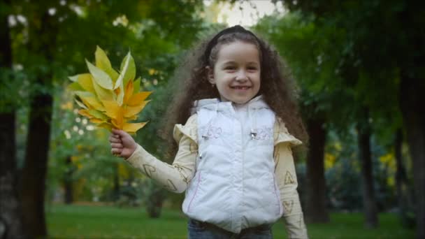 Moda mutlu gülümseyen şık neşeli Avrupa küçük sevimli kız güzel bir beyaz ceket yelek ve uzun sarışın kıvırcık saç yürür Sonbahar Park sahiptir mutlu oynarken ile sonbahar yaprakları, çalışan — Stok video