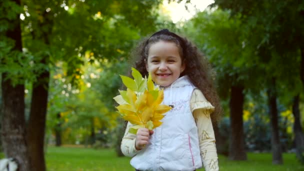 Piękny modne szczęśliwy uśmiechający się stylowe radosny Europejskiej Little Cute Girl w kamizelkę biała kurtka i długo blondynka kręcone włosy spacery w jesieni Park cieszy się chętnie zagram z jesieni pozostawia, systemem — Wideo stockowe