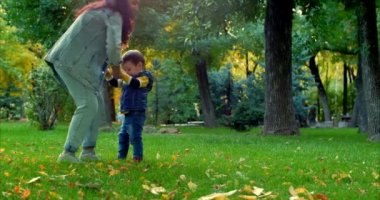 Güzel mutlu gülümseyen şık neşeli Avrupa şirin anne bir kot takım elbise ve bir güzel küçük oğlu iki yıl, anne ve bebek dans ile Sonbahar Park uzun kıvırcık saç yürür. Aile