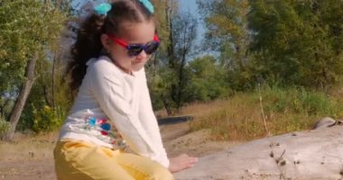 Güzel mutlu şık neşeli Avrupa sevimli küçük kız oturma nehir ve berabere tablette yakınında. 4k