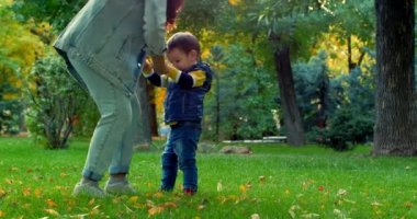 Güzel mutlu gülümseyen şık neşeli Avrupa şirin anne bir kot takım elbise ve bir güzel küçük oğlu iki yıl, anne ve bebek dans ile Sonbahar Park uzun kıvırcık saç yürür. Aile