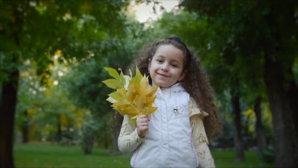 Beautiful Fashionable Happy Smiling Stylish Joyful European Little Cute Girl in a White Jacket Vest and Long Blonde Hair Walks in the Autumn Park Enjoys Happy Playing with Autumn leaves, Running — стоковое видео