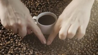 Kahve ve kahve çekirdekleri. Kadın el kahve çekirdekleri kalbinde çizin. Dumanı tüten kahve etrafında kavrulmuş fasulye ile beyaz bir fincan.