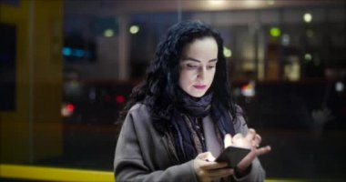 Güzel mutlu genç kadın kahverengi ceket koyu mavi eşarp ve uzun karanlık kıvırcık saç sahiptir kahve meşgul ile onun cep telefonu iken yürüme ile bir şehir sokak. Güzel kız Smartphone 4 k mesajlaşma