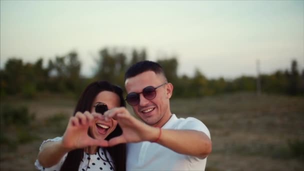 Bonito feliz elegante jovem europeu bonito casal nos braços um do outro, faz fora das mãos de uma ideia romântica de amor na forma de um coração. Conceito de Amor . — Vídeo de Stock