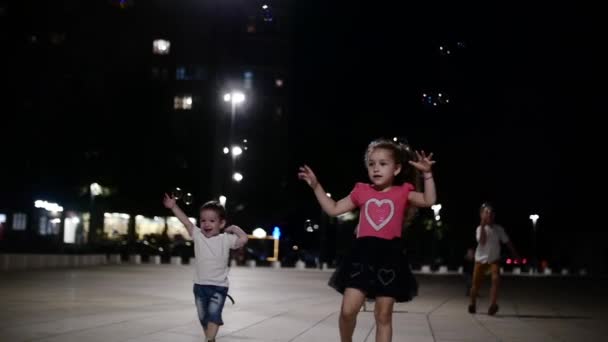 Grupo feliz de crianças brincando no parque com bolhas de sabão. Crianças pegam bolhas de sabão à noite no parque . — Vídeo de Stock