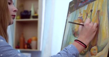 Genç güzel kadın sanatçı bir sanat stüdyosu, bir şövale arkasında oturan ve tuval üzerine resim mevcuttur. Çizim işlemi: sanatçılar sanat stüdyoda el sanat kız ile Canvas.4k bir fırça boyama