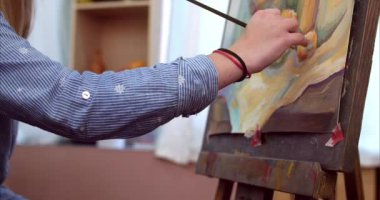 Genç güzel kadın sanatçı bir sanat stüdyosu, bir şövale arkasında oturan ve tuval üzerine resim mevcuttur. Çizim işlemi: sanatçılar sanat stüdyoda el sanat kız ile Canvas.4k bir fırça boyama