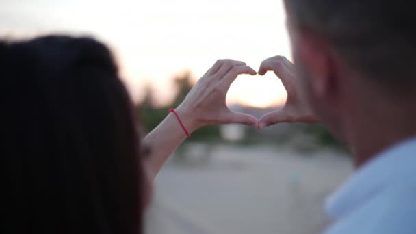 Mooie gelukkige stijlvolle vrolijke jonge Europese schattig paar in de armen van elkaar, maakt uit de handen van een romantisch idee van liefde in de vorm van een hart. Concept van liefde. — Stockvideo