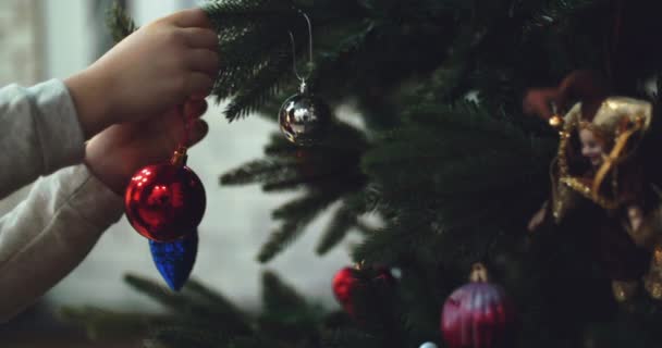 Повесить рождественское украшение на елку с рождественскими огнями. Украшение рождественской елки мячом. 4K — стоковое видео
