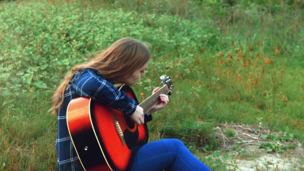 Ein junges simpotichnaya Mädchen stimmt die Gitarre, sie ist traurig einsam, wenn die Sonne über dem Horizont untergeht. 4k. — Stockvideo