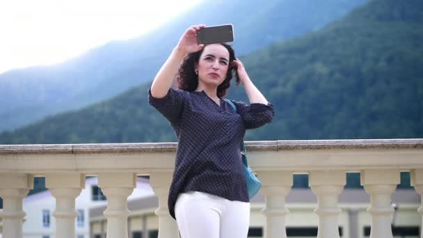 Smart, beautiful brunette corrects curly hair and talks on the phone by Skype on the background of outstanding mountains and beautiful sunset. — Stock Video