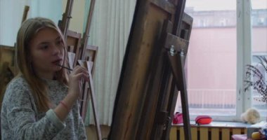 Genç güzel kadın sanatçı bir sanat stüdyosu, bir şövale arkasında oturan ve tuval üzerine resim mevcuttur. Çizim işlemi: sanatçılar sanat stüdyoda el sanat kız ile Canvas.4k bir fırça boyama