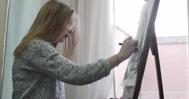 Joven artista femenina hermosa está en un estudio de arte, sentado detrás de un caballete y pintura sobre lienzo. Proceso de Dibujo: en el Estudio de Arte de la Mano de los Artistas Chica de Arte con Pincelada sobre Lienzo.4K — Vídeos de Stock