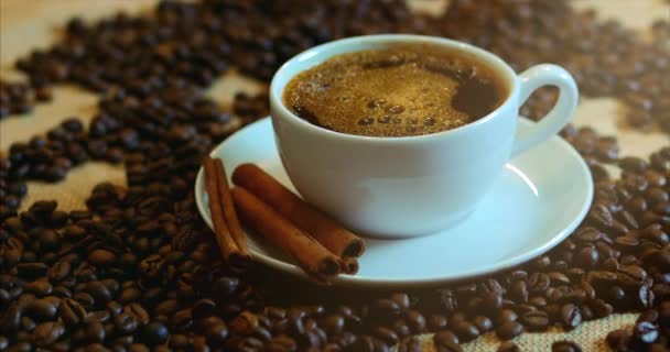 Kahve ve kahve çekirdekleri. Kahve kavrulmuş fasulye ile masada buharlaşan bir beyaz fincan. Stok görüntüleri 4k. — Stok video