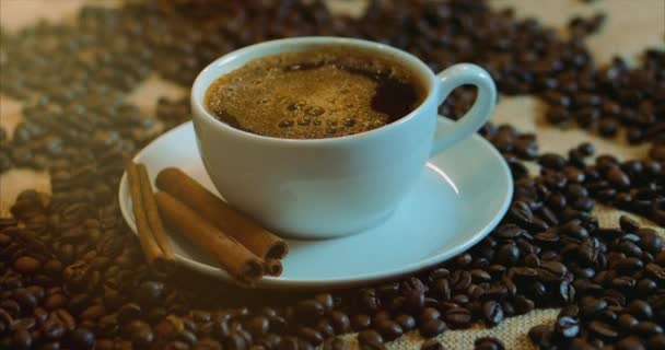 Taza de café y granos de café. Una taza blanca de café evaporando sobre la mesa con frijol asado. Imágenes de archivo 4k . — Vídeo de stock
