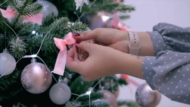 若い女性の手 お祭りのライトとクリスマスのお祝いクリスマス ツリーを飾るクリスマス ツリーに弓を普及 — ストック動画
