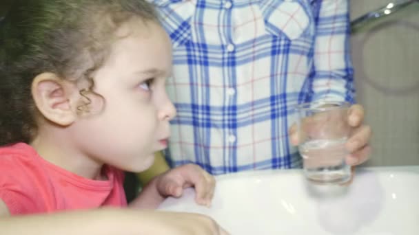 Mädchen putzt sich nach dem Essen vorsichtig die Zähne. Mama bringt ihrer Tochter bei, wie man nach dem Essen den Mund reinigt und spült. 4k. — Stockvideo